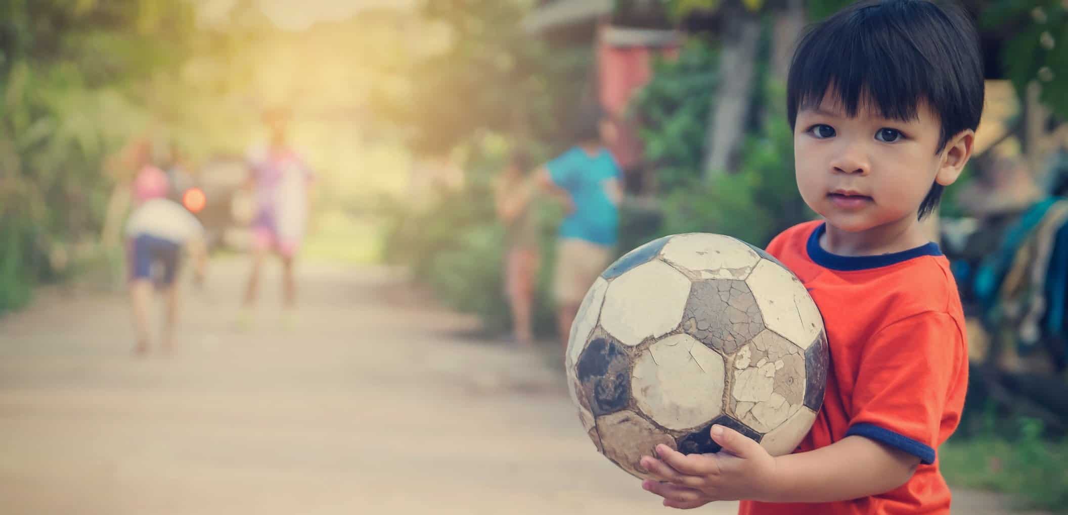 Poor Asian Boy Playing With Old Rustic Soccer Ball