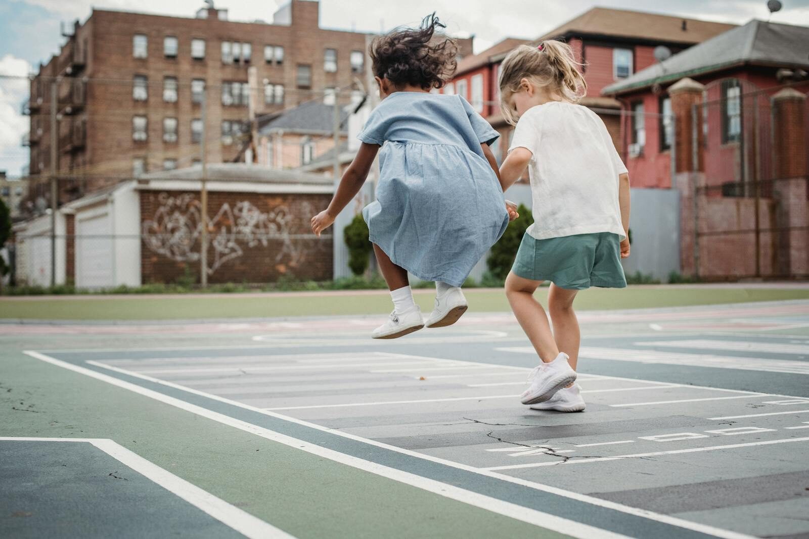 Two young girls jumping and playing together on a city playground.