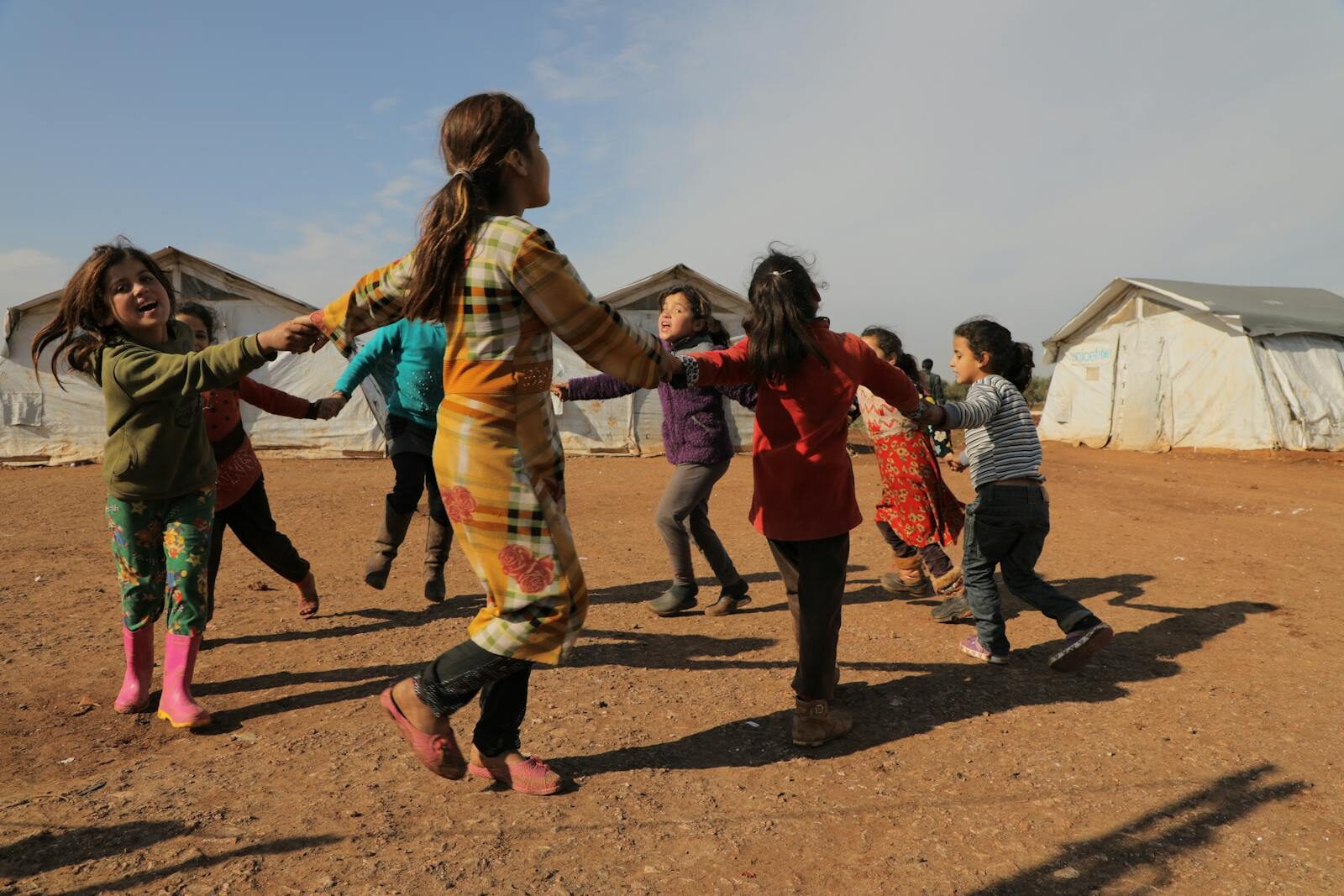 Children joyfully play outdoors in a Syrian refugee camp, forming a lively circle.